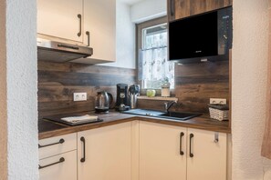 A modern kitchen with wooden cabinetry, a stainless steel range hood, a built-in microwave, and a window with a view.