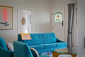 A living room with a teal sofa, a glass coffee table, and a door with a green stained glass window.