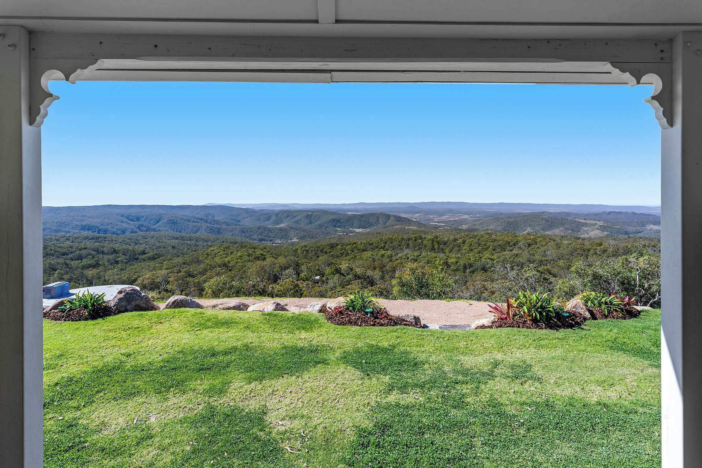 A view from a covered outdoor area with a clear sky, a grassy lawn, and a distant hilly landscape.
