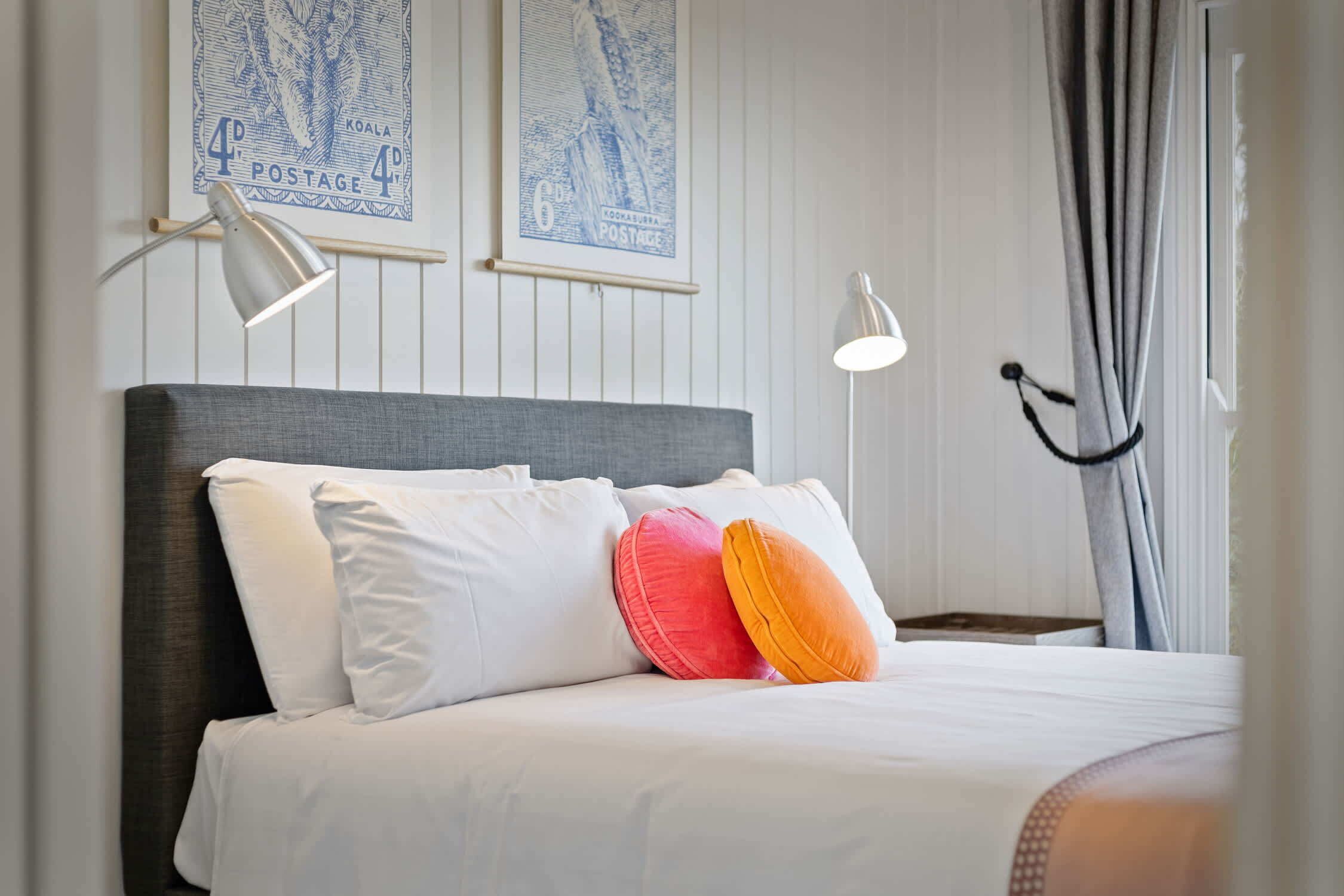 A neatly made bed with white and colorful pillows, a grey headboard, and two wall-mounted reading lamps.