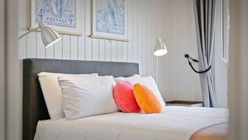 A neatly made bed with white and colorful pillows, a grey headboard, and two wall-mounted reading lamps.