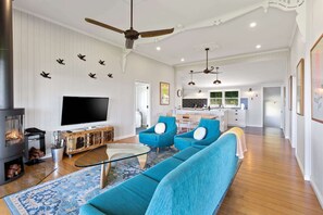 A spacious living room with a large flat-screen TV, a fireplace, and a modern kitchen in the background.