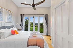 A bedroom with a bed, a ceiling fan, a view of the outdoors through a glass door, and a framed picture on the wall.