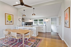 A modern kitchen with white cabinetry, a wooden dining table, and a ceiling fan.
