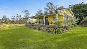 Une maison jaune avec un porche, entourée d’une pelouse bien entretenue et d’arbres.