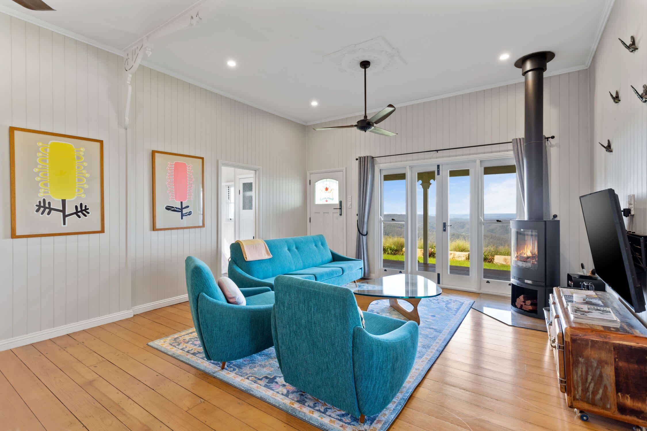 A spacious living room with a blue sofa set, a fireplace, and a view through large glass doors.