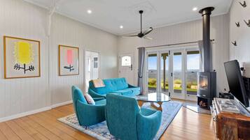 A spacious living room with a blue sofa set, a fireplace, and a view through large glass doors.