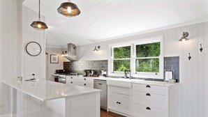 Une cuisine moderne avec des meubles blancs, un îlot central, une cuisinière et une fenêtre donnant sur un espace verdoyant.