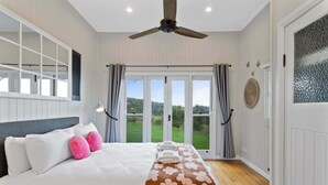 Une chambre à coucher avec un lit, des rideaux, un ventilateur de plafond et une vue sur l’extérieur.