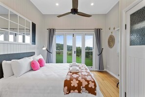 A bedroom with a bed, curtains, a ceiling fan, and a view of the outdoors. - The Quince Cottage - 3 Bedrooms (Ravensbourne)