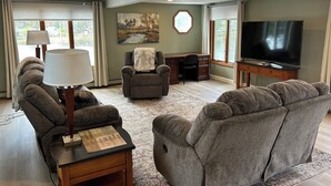 Een woonkamer met een plafondventilator, een televisie, een bureau en twee fauteuils.
