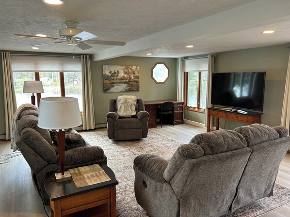 A living room with a ceiling fan, a television, a desk, and two armchairs.