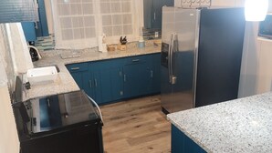 A kitchen with blue cabinets, a black refrigerator, and a wooden ceiling. - Location Location Location! Classic Beach Cottage less than 1-min walk to beach! (Murrells Inlet)