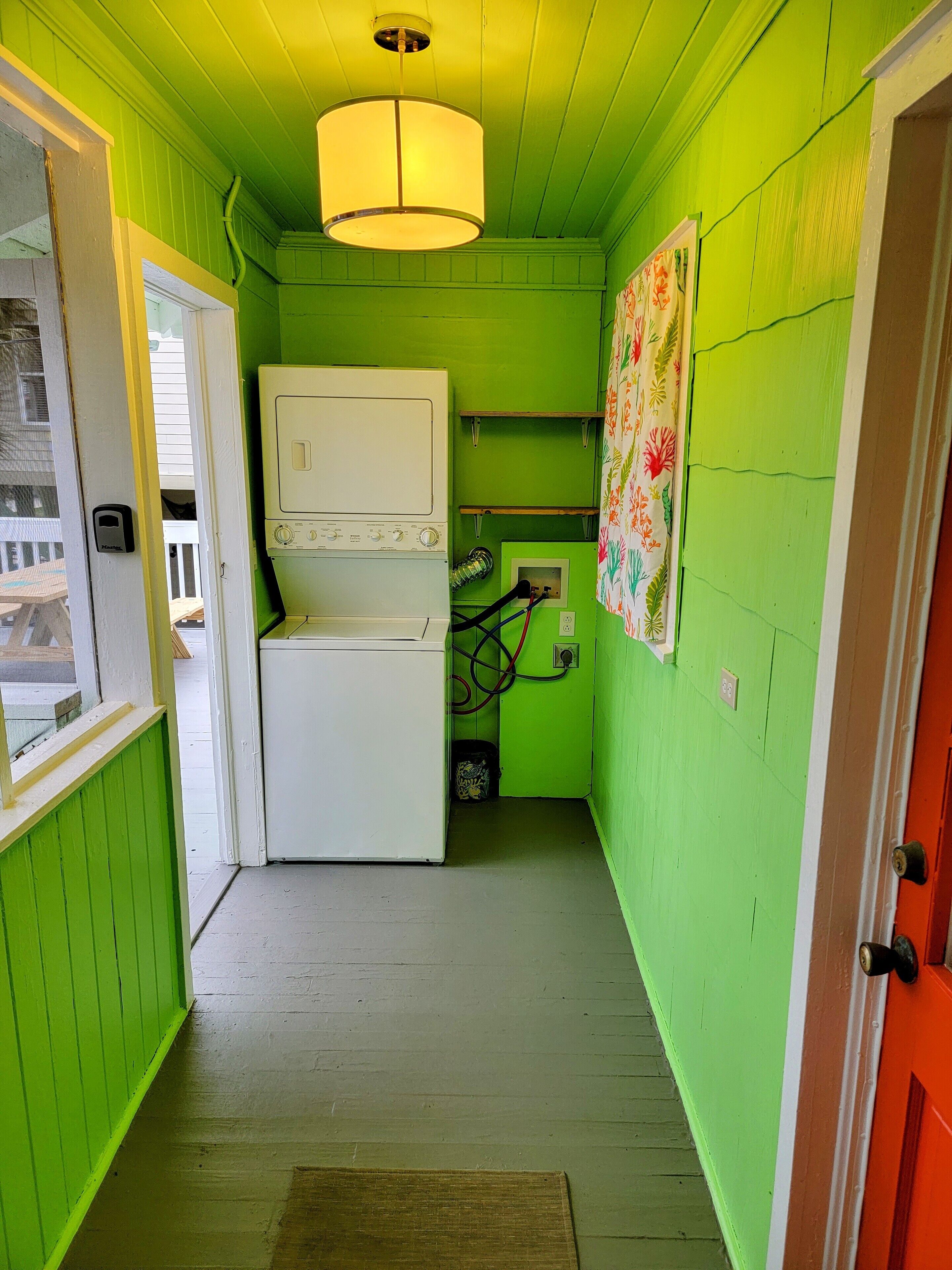 A narrow hallway with green walls and a white washing machine. There is a door on the left and a red door on the right.