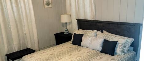 A bedroom with a bed, a nightstand, a lamp, and a bench.