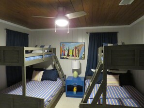 Una habitación con literas, ventilador de techo, un cuadro y una pequeña mesa con lámpara.