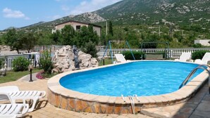Una piscina con borde de piedra, rodeada de sillas de descanso blancas y una pequeña formación rocosa.