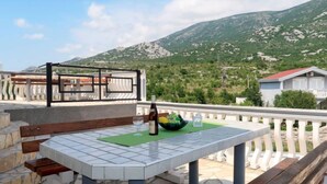 Una terraza con mesa, sillas y vistas a un paisaje montañoso.
