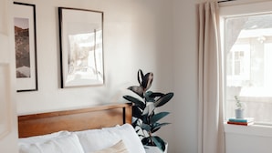 Una cama bien hecha con cabecera de madera, una planta en maceta y dos cuadros en la pared.