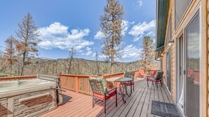 A wooden deck with a hot tub, outdoor seating, and a view of trees and hills.