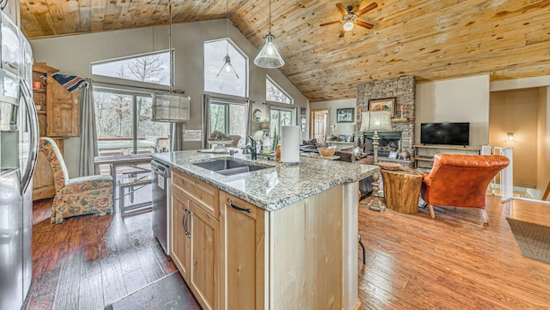 A spacious kitchen with a large island, wooden ceiling, and a stone fireplace.