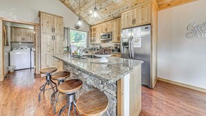 A kitchen with wooden cabinets, granite countertops, a stainless steel refrigerator, and a bar stool area.