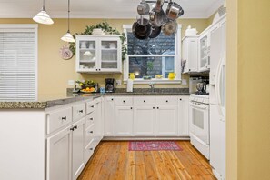Una cocina con gabinetes blancos, encimera de granito, ventana con vistas y una percha para ollas.