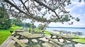Terraza de madera con mesas de picnic y vista a un lago con barcos.
