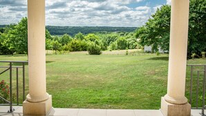 A covered outdoor area with columns, a grassy lawn, and a view of a forested landscape. - Nice villa with private pool and pool house (Montaigu de Quercy)