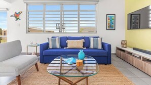 Un salon moderne avec un canapé bleu, une table basse en verre et une planche de surf accrochée au mur.