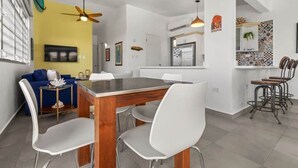 Une cuisine moderne avec un coin repas, comprenant une table en bois, des chaises blanches et des ventilateurs de plafond.