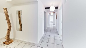 Een moderne hal met witte wanden, een betegelde vloer en een houten sculptuur.