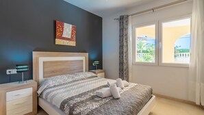 A bedroom with a bed, bedside tables, a wall art piece, and a window with curtains. - Villa Cucarres with sea and mountain views, Wi-Fi, air conditioning, and garden (Calpe)