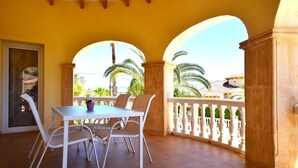 A covered patio with a table and chairs, a view of palm trees, and a balcony railing. - Villa Cucarres with sea and mountain views, Wi-Fi, air conditioning, and garden (Calpe)