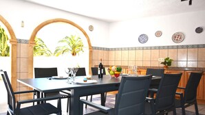 A dining area with a table set for six, chairs, a bottle of wine, and a fruit bowl. - Villa Cucarres with sea and mountain views, Wi-Fi, air conditioning, and garden (Calpe)