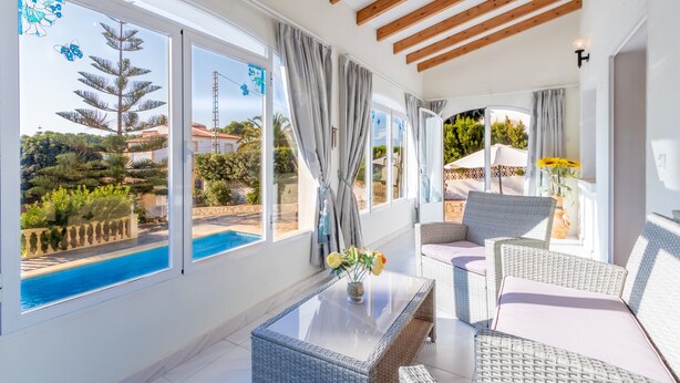 A sunlit room with large windows, wicker furniture, and a view of a swimming pool. - Villa Rosa with mountain views, pool, Wi-Fi, air conditioning, terrace and garden (Benissa)