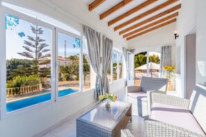 A sunlit room with large windows, wicker furniture, and a view of a swimming pool. - Villa Rosa with mountain views, pool, Wi-Fi, air conditioning, terrace and garden (Benissa)