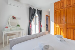 Une chambre à coucher avec un lit, une table de chevet avec un miroir, une commode et une fenêtre avec des rideaux.
