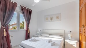 A bedroom with a bed, nightstands, a window with curtains, a wall-mounted artwork, and a wooden door. - Villa Rosa with mountain views, pool, Wi-Fi, air conditioning, terrace and garden (Benissa)