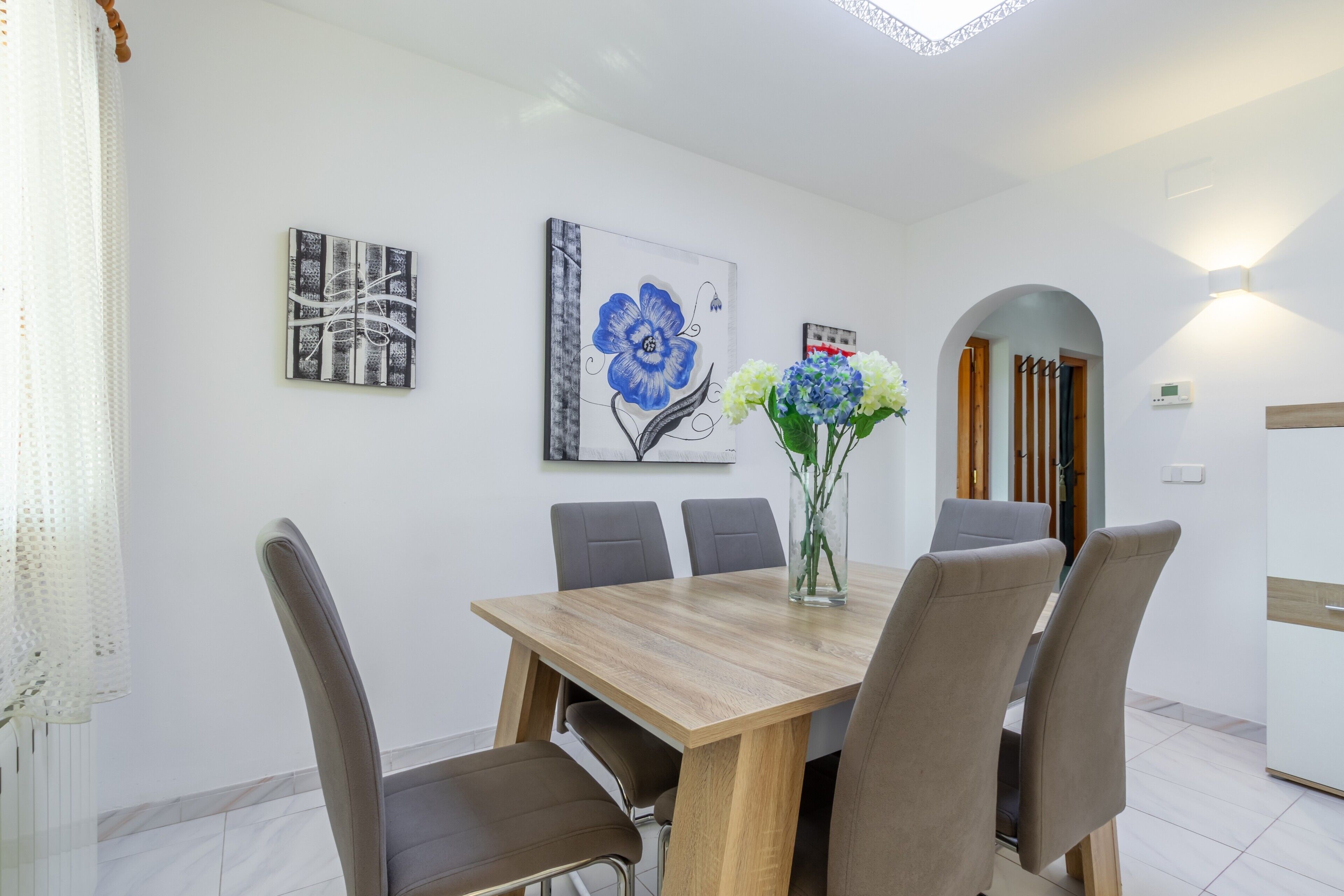 A dining area with a wooden table, six chairs, and two wall-mounted paintings.