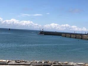 A coastal scene with a pier extending into calm waters, a small boat near the pier, and a distant ship on the horizon. - A pleasant, comfortable apartment with a view of the sea (Granville)