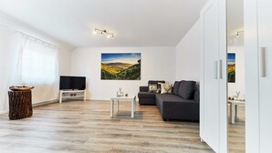 A modern living room with a flat-screen TV, a gray sofa, a coffee table, and a painting of a landscape. - Large, beautiful vacation apartment with 2 bedrooms (Ettenheim)