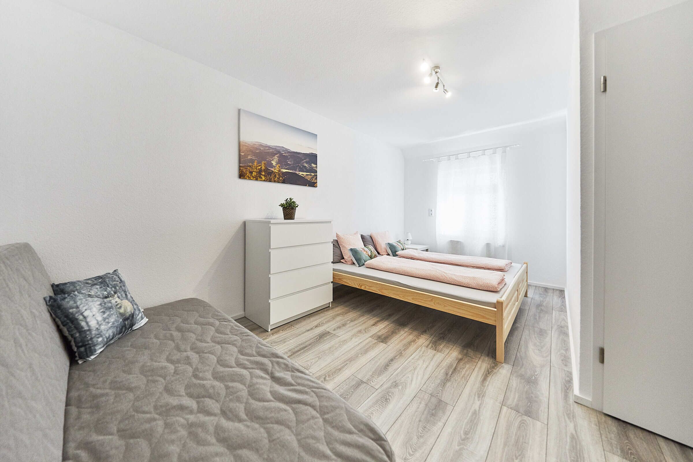 Ein modernes Schlafzimmer mit Bett, Sofa, Schminktisch und einem Fenster mit Vorhängen.