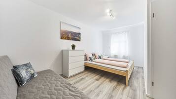 Ein modernes Schlafzimmer mit Bett, Sofa, Schminktisch und einem Fenster mit Vorhängen.