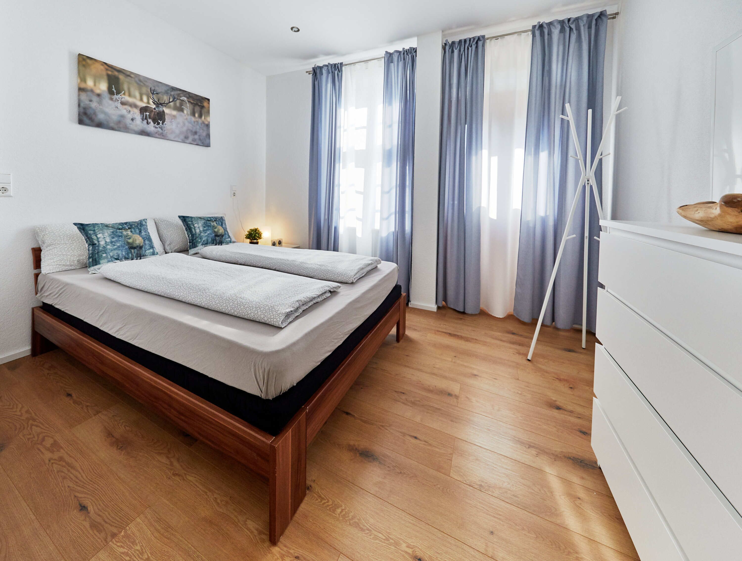 A bedroom with a wooden bed, a white dresser, and a painting of a deer on the wall.