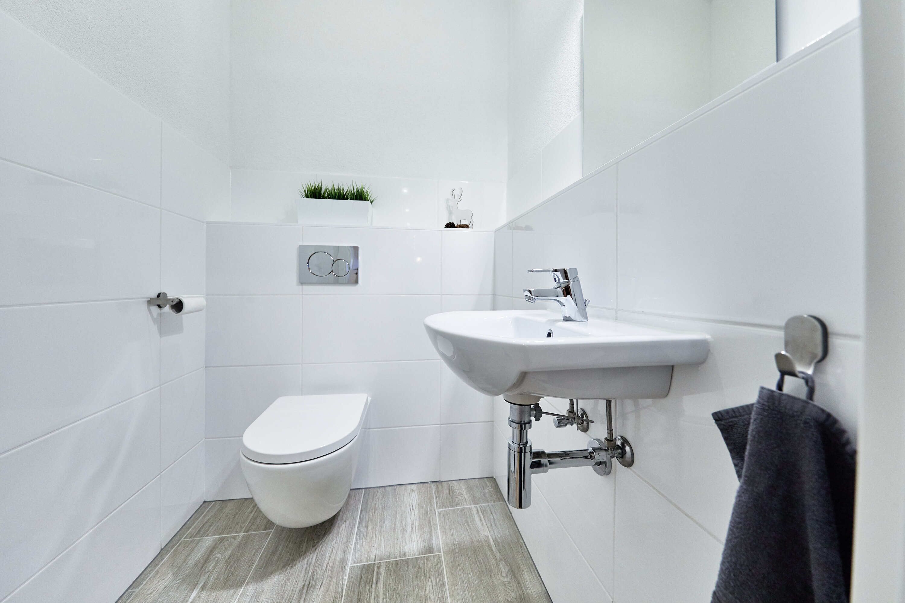 A modern bathroom with white tiles, a white toilet, a sink with a mirror, and a towel hanging on a rack.