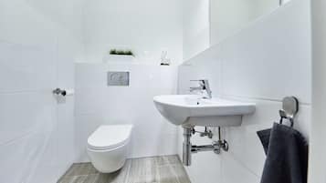 A modern bathroom with white tiles, a white toilet, a sink with a mirror, and a towel hanging on a rack.