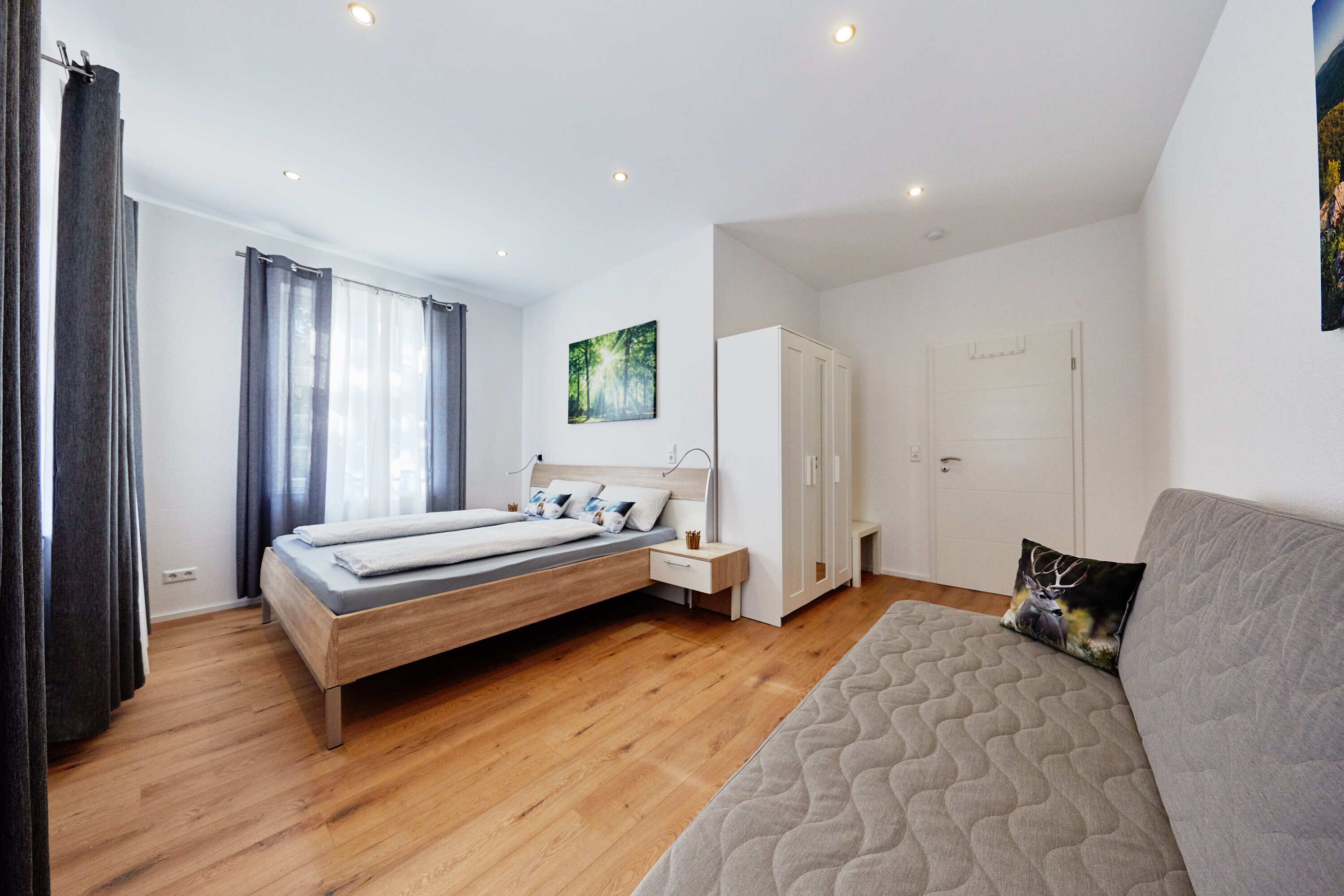 A modern bedroom with a bed, bedside table, wardrobe, and a sofa.