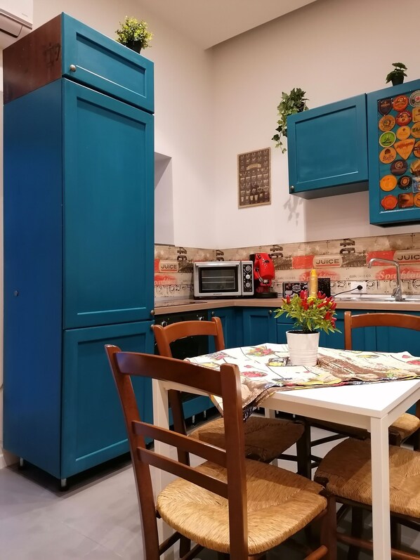 Een keuken met blauwe kastjes, een magnetron, een broodrooster en een tafel met stoelen.