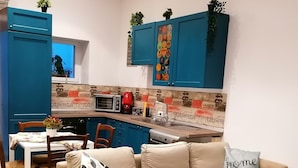 Un salon moderne avec un canapé d’angle beige, une table à manger avec des chaises et un coin cuisine doté de meubles bleus et d’un revêtement mural.